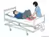 Bild som visar hur patienten ligger på rygg i sängen och  får hjälp av en vårdpersonal att sätta sina fötter på en glidmatta. 