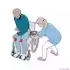 Bild som beskriver hur en vårdpersonal för in en glidskiva under låren på patienten som sitter i rullstolen. 